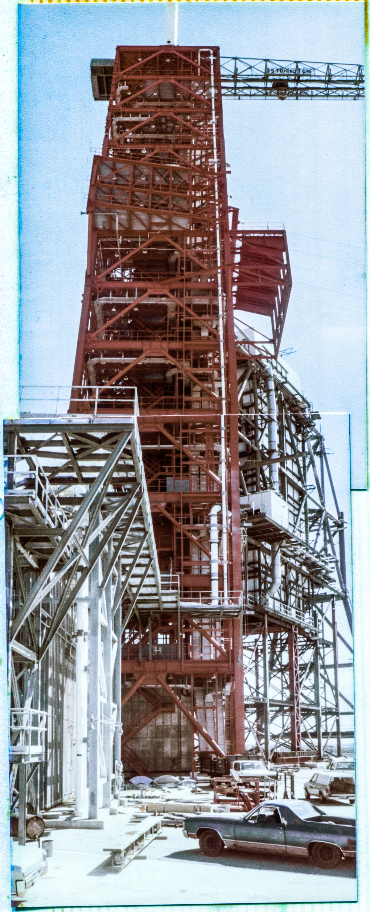 Image 013. The Fixed Service Structure at Space Shuttle Launch Complex 39-B, Kennedy Space Center, Florida, towers into the sky above you, viewed from due north of it, nearby, on the Pad Deck. The FSS was created by reusing most of the Launch Umbilical Tower from Mobile Launcher 3, which was originally built to service Saturn V’s as part of the Apollo Program. In this photomontage, taken during the early phases of the Space Shuttle modifications to Pad B, the FSS retains its original red paint job, prior to it being sandblasted and repainted gray, which color it retained for the duration of the Space Shuttle Program. Photo by James MacLaren.